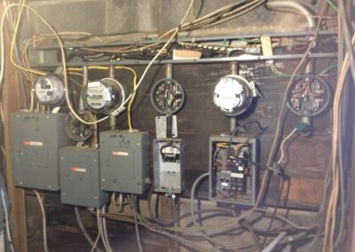 A wall-mounted electrical panel with multiple meters and wiring, including circuit breakers and various cables in an industrial setting.