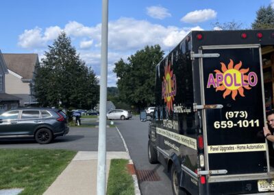 A black utility truck with "Apollo" and contact information is parked on a residential street near a black SUV. A sidewalk and lamppost are visible under a clear blue sky with clouds.